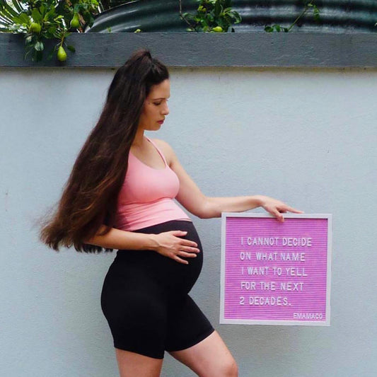 Pregnant woman in second trimester boxing in a park wearing black maternity bike shorts and sports bra