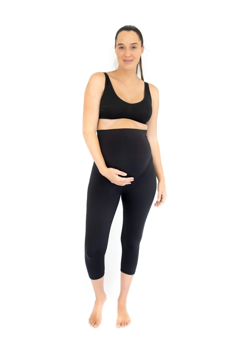 New mother in black and white activewear sitting on a pink bench eating pancakes with strawberries and blueberries.